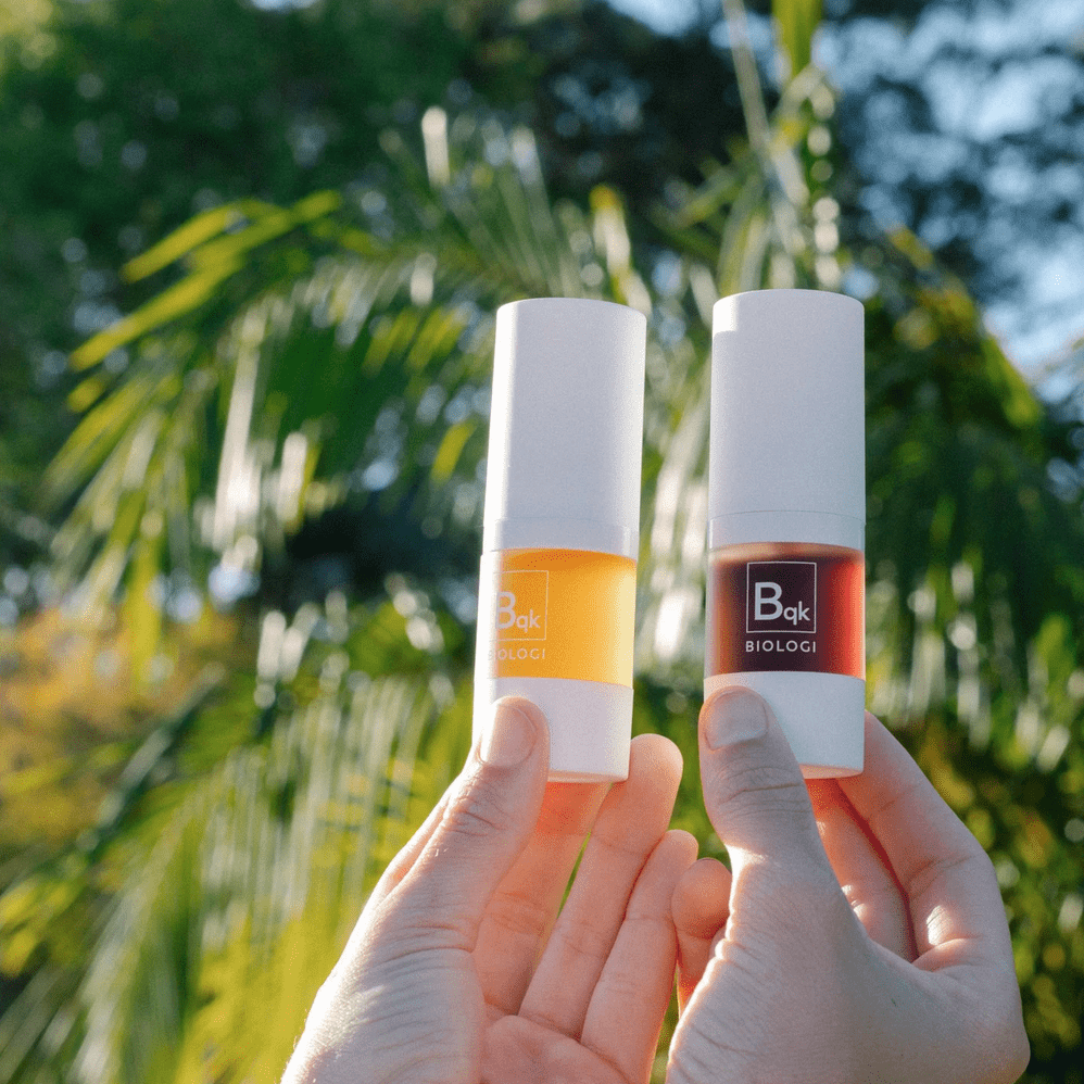 Two hands holding up two biologi products in front of some trees in the background