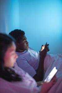 Two people laying in bed on their phones with a blue light in the background