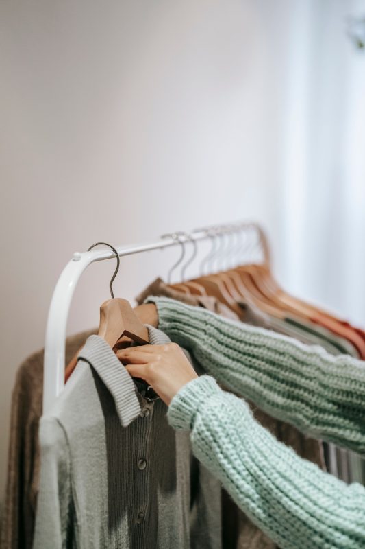 A person checking the label of a shirt hanging a rack of clothing to know if it is fast fashion or sustainable clothing