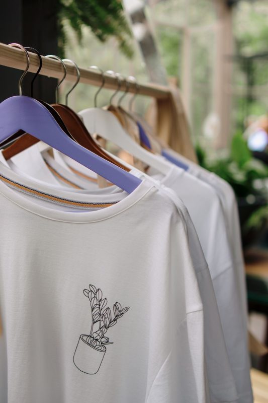 White shirts with a plant logo hanging on a clothing rack