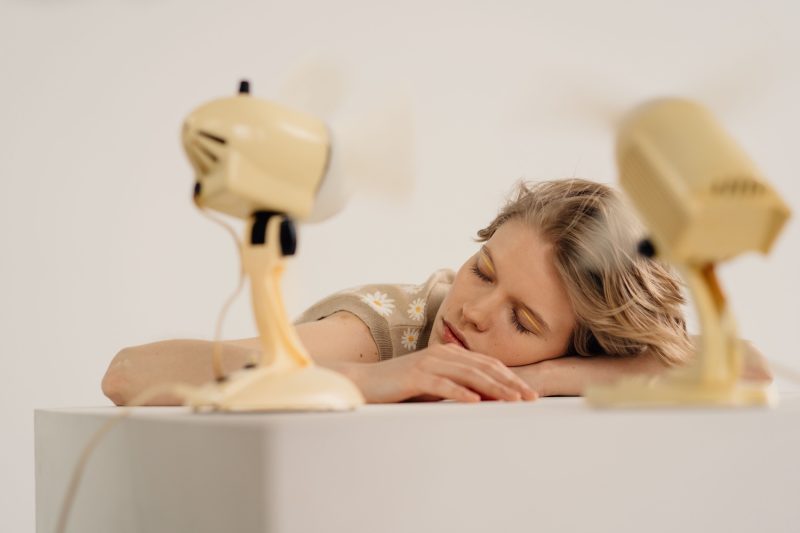 Woman laying her arms and head on a table in front of 2 fans